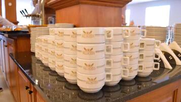 Varias tazas blancas con emblemas dorados sobre una encimera de cocina.