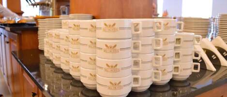 Varias tazas blancas con emblemas dorados sobre una encimera de cocina.