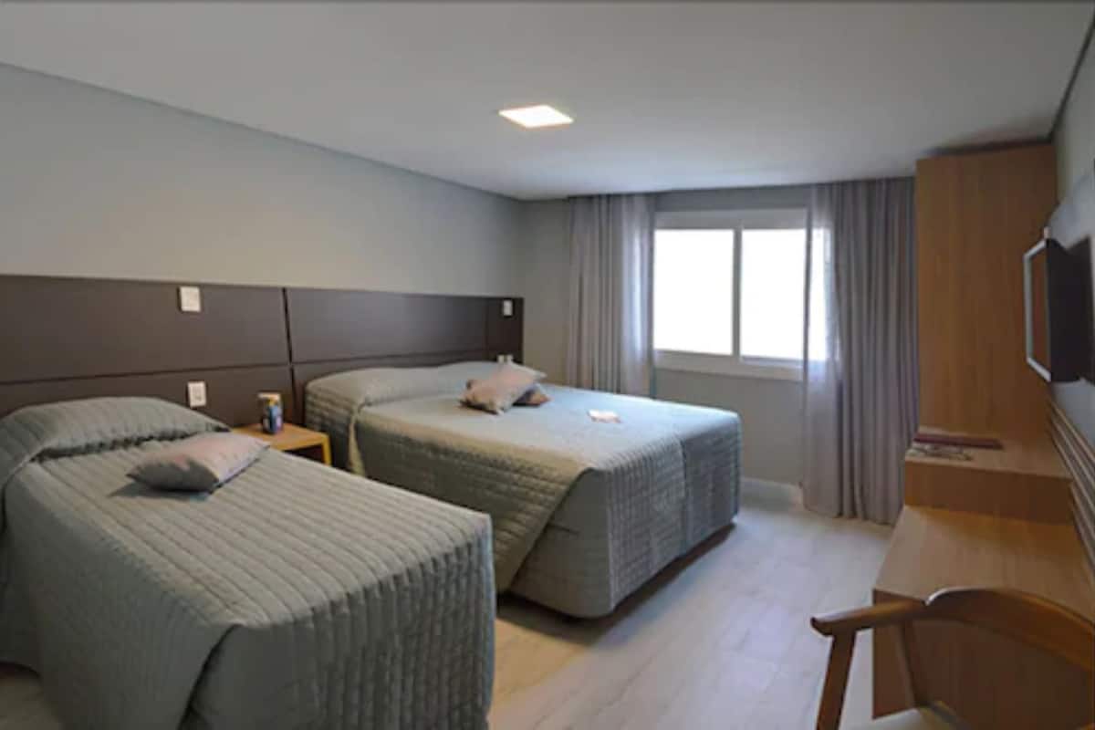 A hotel room with two beds, a desk, a chair, a TV, and a window with curtains.