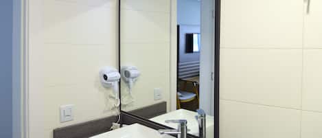 Une salle de bain avec un lavabo blanc, un miroir et deux sèche-cheveux fixés au mur.