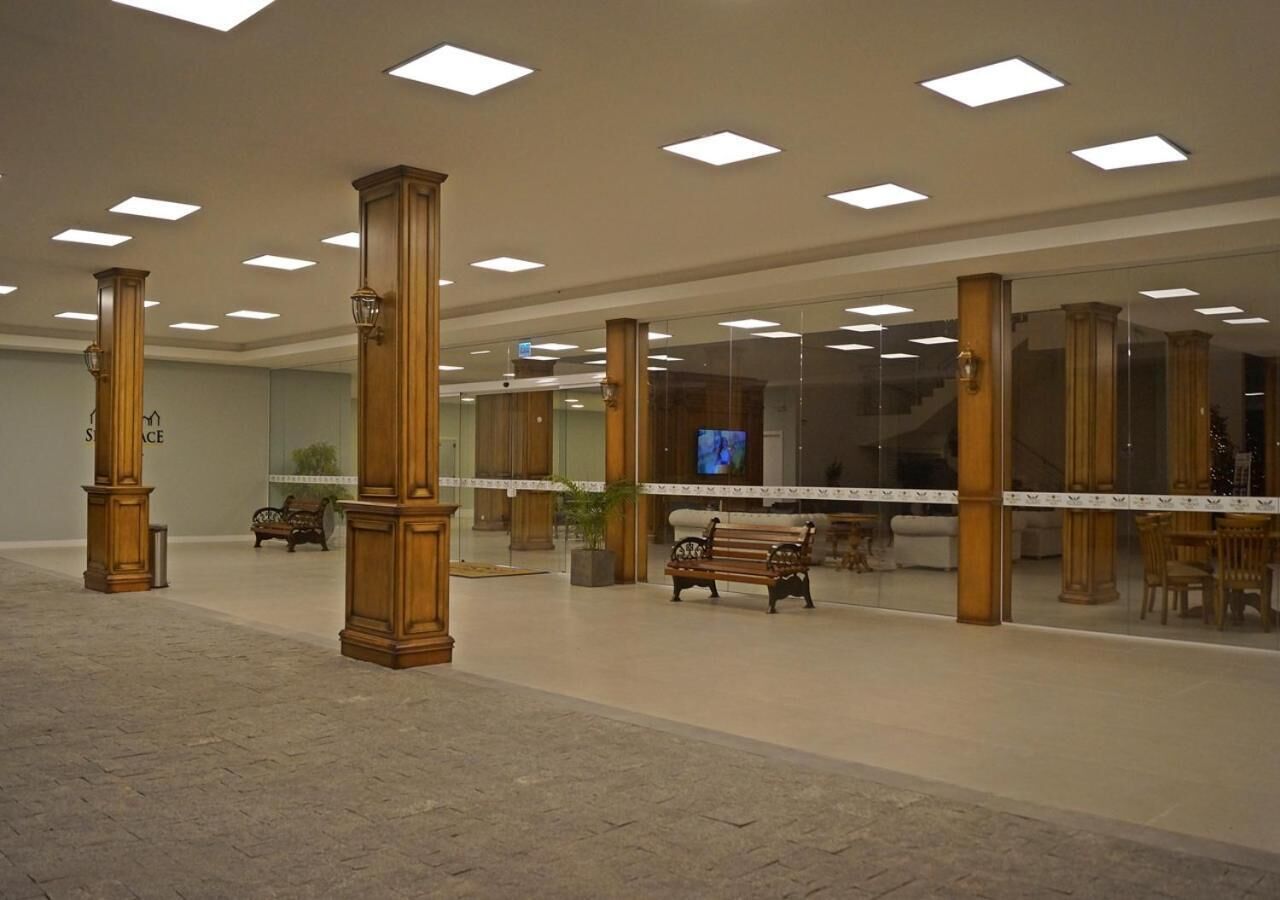 Un hall d’entrée spacieux avec de hauts plafonds, des colonnes en bois, un banc central et un écran de télévision.