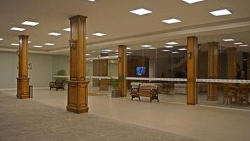 A spacious lobby with high ceilings, wooden columns, a central bench, and a television screen.