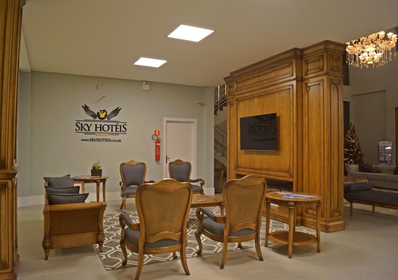 A hotel lobby with a reception desk, a seating area with wooden chairs and tables, a Christmas tree, and a staircase.