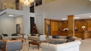 A spacious lobby with a high ceiling, a staircase, and a Christmas tree. There are multiple seating areas with sofas and a reception desk. - Sky Palace Hotel (Gramado)