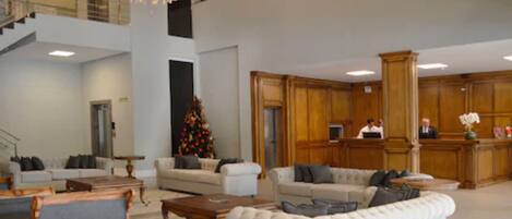 Un vestíbulo amplio con techo alto, una escalera y un árbol de Navidad. Hay varias zonas de estar con sofás y un mostrador de recepción.