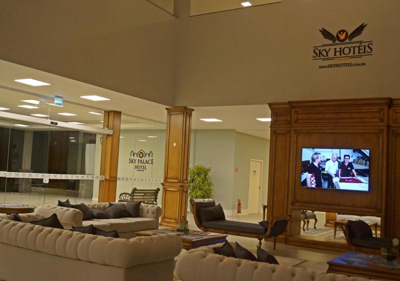 A hotel lobby with a large sofa, armchairs, a television, and a sign for Sky Palace Hotel.