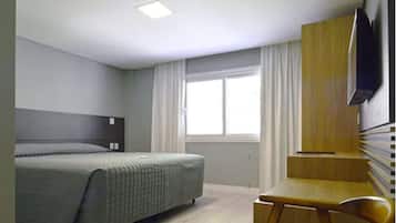 A modern hotel room with a bed, a desk, a chair, a TV, and a window with curtains.