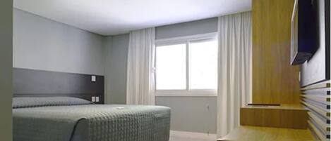 Una habitación de hotel moderna con una cama, un escritorio, una silla, un televisor y una ventana con cortinas.