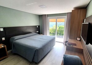 A hotel room with a bed, a TV, a small table, and a balcony with a view of greenery. - Sky Palace Hotel (Gramado)