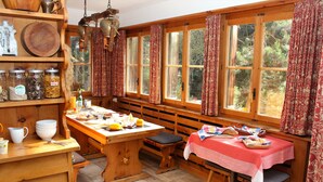 A rustic kitchen with wooden shelves, a central island, and large windows with curtains. - B&B Arche de Noé (Bagnes)