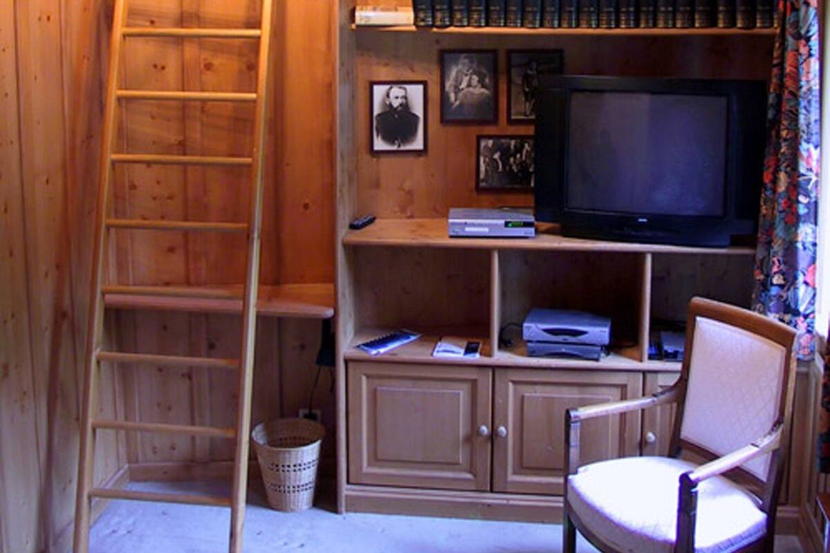 A wooden cabin interior with a bookshelf, television, and a chair.