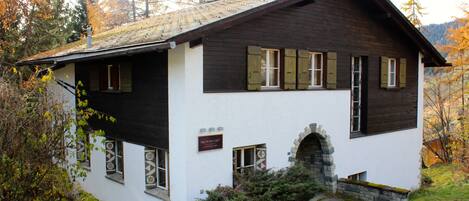 Ein traditionelles Chalet mit steilem Walmdach, Holzfassade und einem steinernen Bogenportal.
