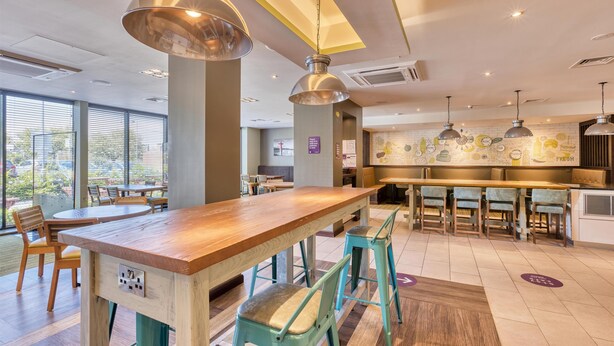 Et moderne restaurantmiljø med en træbar, teal stole, hængende lys og udsigt gennem store vinduer.