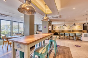 A modern restaurant interior with a wooden bar, teal chairs, pendant lighting, and a view through large windows. - Premier Inn Bangor - Northern Ireland (Bangor)