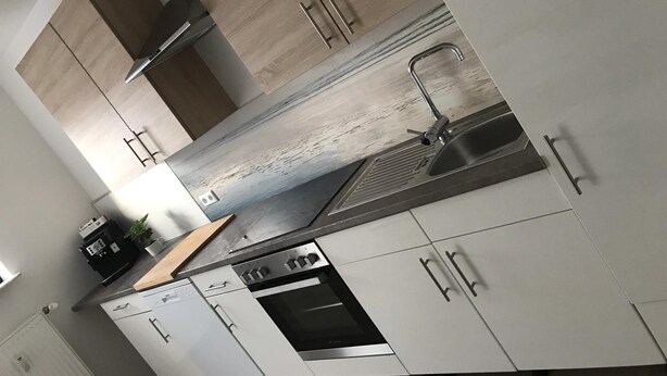 A modern kitchen with white cabinetry, a stainless steel sink, and a built-in oven. - Ferienwohnungen AKH Home (Sankt Wendel)