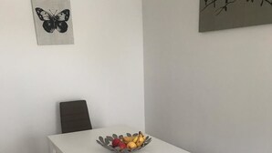 A dining area with a white table, four chairs, a fruit bowl, and two wall art pieces. - Ferienwohnungen AKH Home (Sankt Wendel)