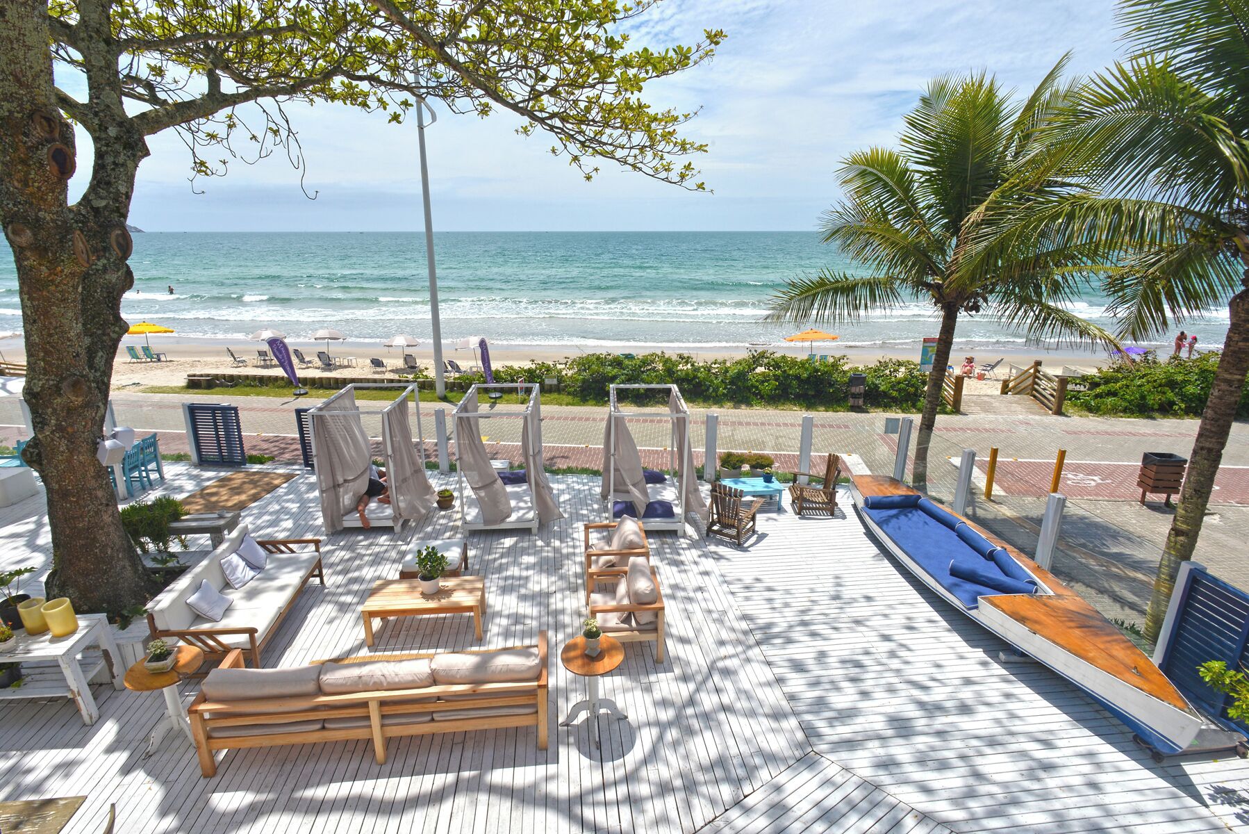 Une terrasse en bois avec des meubles d’extérieur, notamment des canapés et des fauteuils, donnant sur une plage et l’océan.