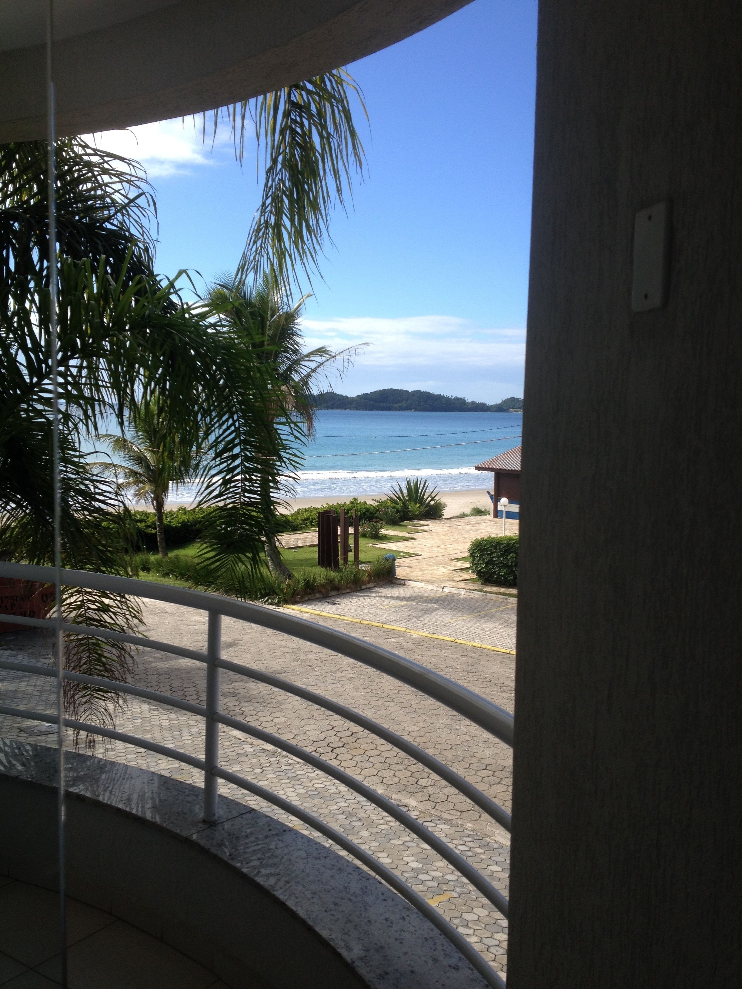 A balcony with a view of the beach, palm trees, and a distant island.