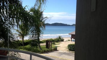 A balcony with a view of the beach, palm trees, and a distant island.