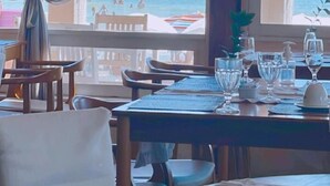 Un comedor con una mesa preparada para dos, con vistas a una playa donde se ven personas a lo lejos.