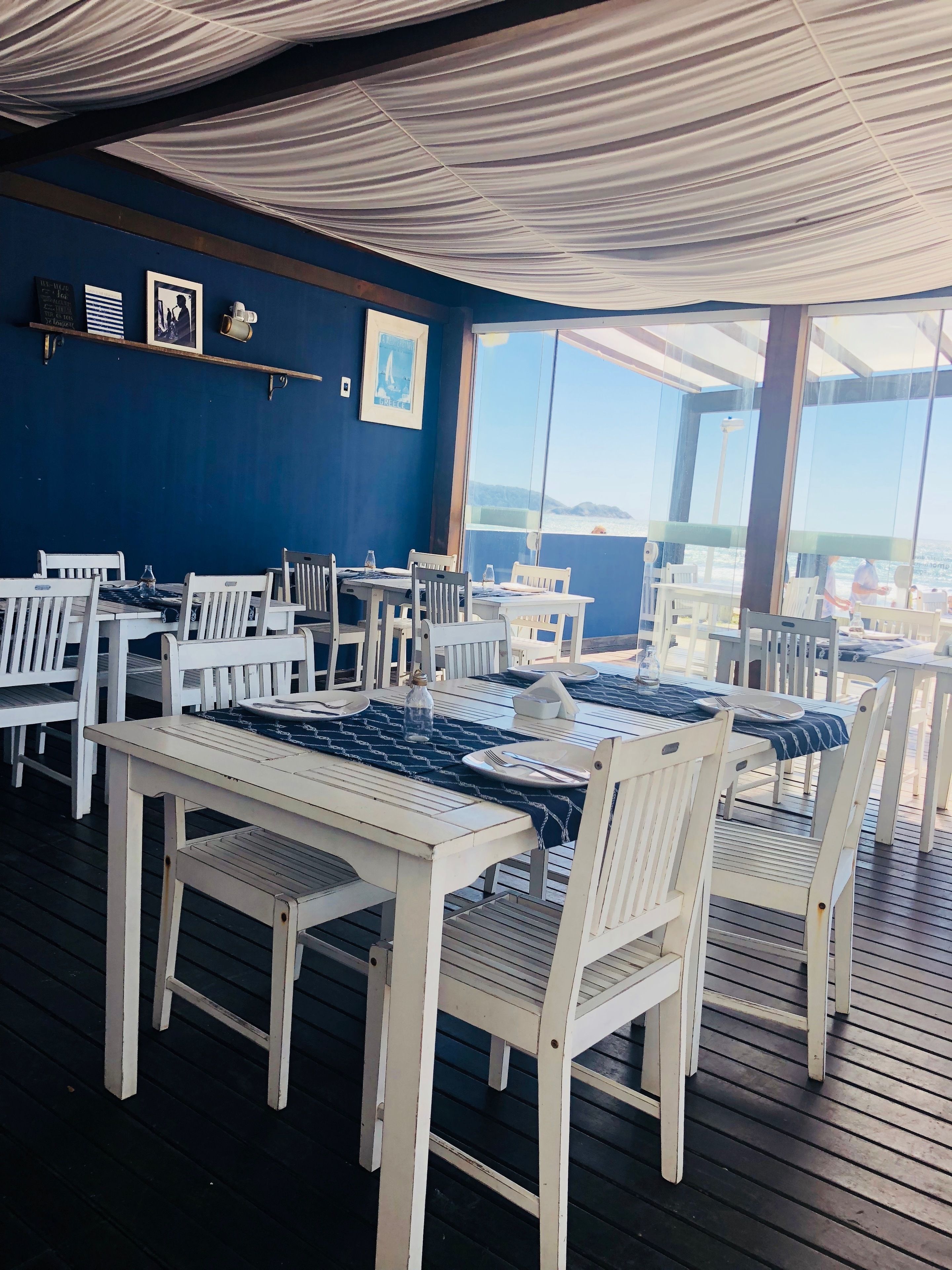 Ein Restaurant mit weißen Holztischen und -stühlen, einer blauen Wand und gerahmten Bildern.