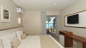 Habitación de hotel con cama, escritorio, televisor y vista a la playa.