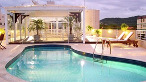 Una piscina con cerramiento de vidrio, sillas de descanso y plantas en macetas.