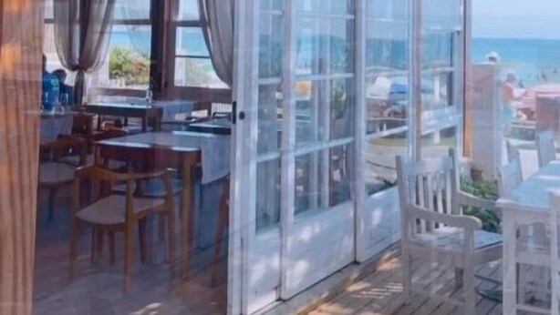 Un espacio de estar techado al aire libre con piso de madera y puertas de vidrio que dan a vistas del mar.