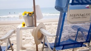 Una silla de playa con una toalla y un cubo con flores, un sombrero de sol y un cartel que dice "MAUNA & LANI Donsada e Lazer".