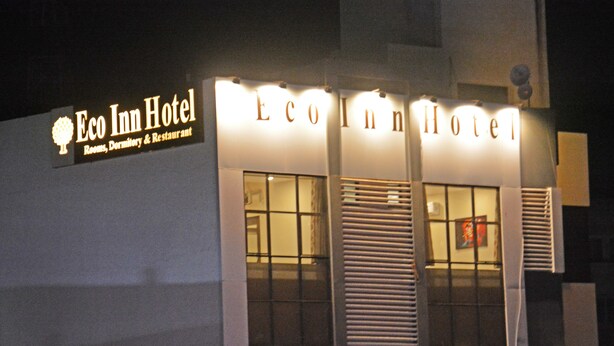 L’extérieur de l’hôtel Eco Inn, avec son enseigne lumineuse, ses grandes fenêtres et son unité de climatisation bien visible.