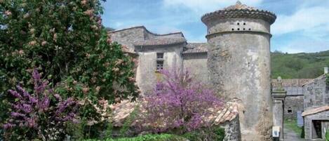A stone building with a tower, surrounded by greenery and a stone wall.