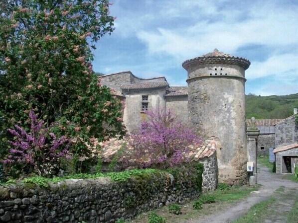 A stone building with a tower, surrounded by greenery and a stone wall. - Domaine du Clap (Pranles)