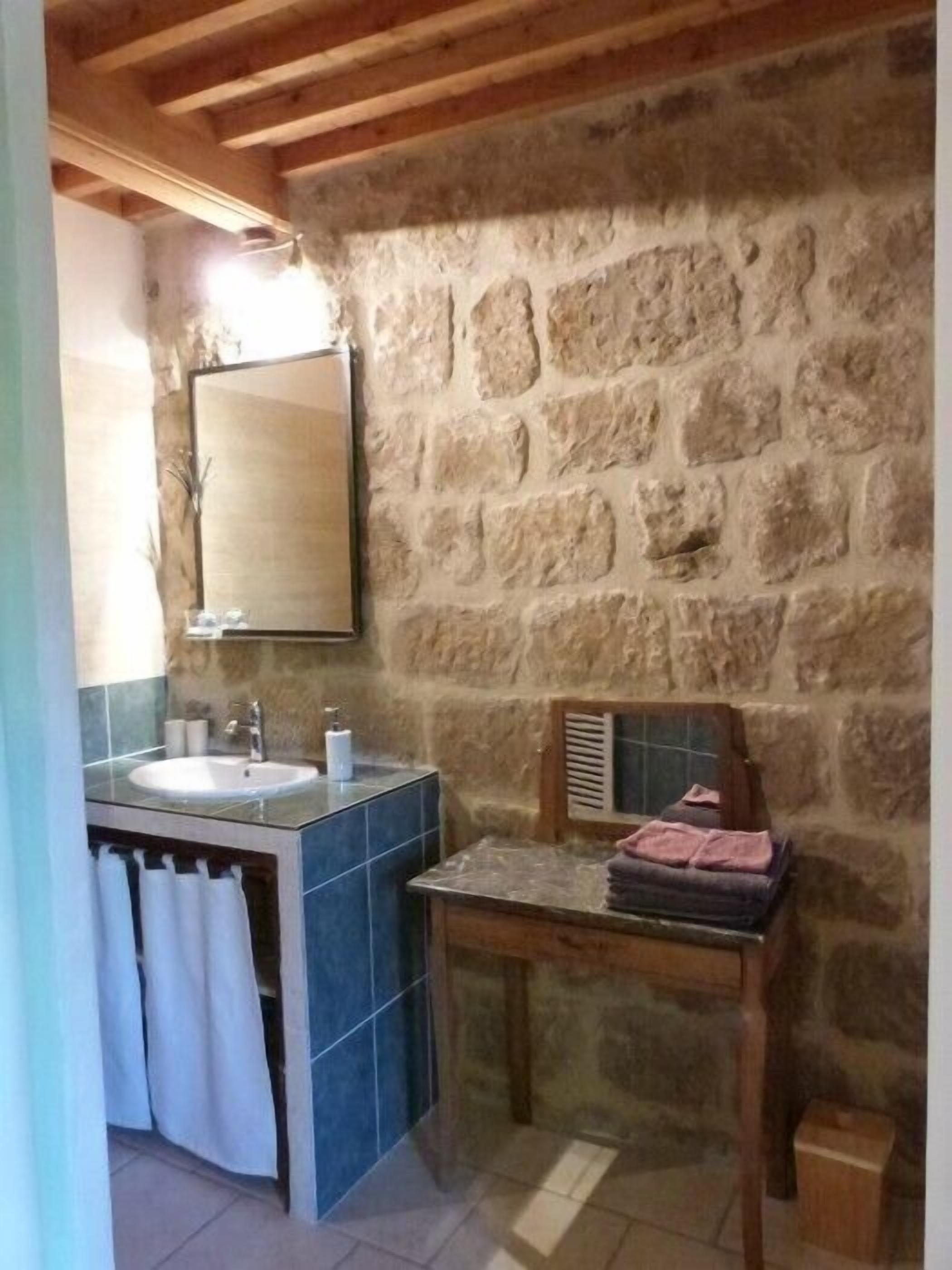 A bathroom with a stone wall, a sink, a mirror, and a towel rack.