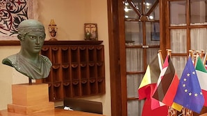 A reception desk with a bust sculpture, a radiator, and multiple flags. - Hotel Apollo (Delphi)
