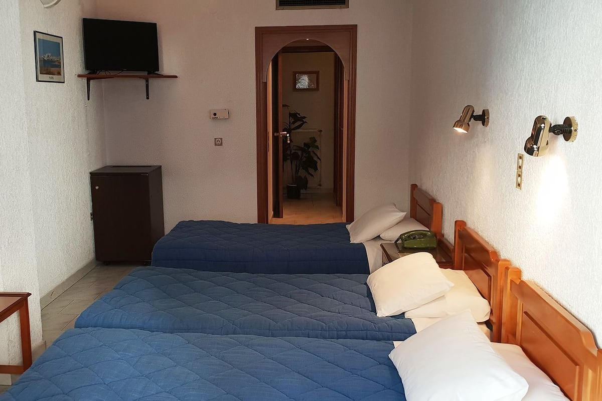 Una habitación pequeña y acogedora con dos camas, un televisor, una mesita y una puerta que da a otra habitación.