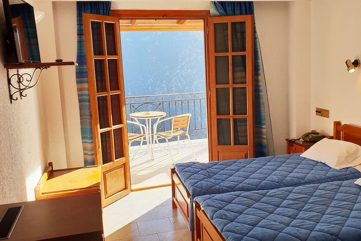 Habitación de hotel con cama, escritorio, silla y balcón con vistas.