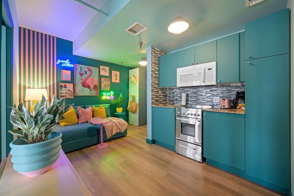 A modern kitchen with teal cabinets, a microwave, and a stove. There is a neon sign on the wall and a plant on the counter.