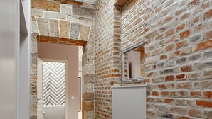 A narrow hallway with a brick wall, a white door with a chevron pattern, and a light wooden floor.