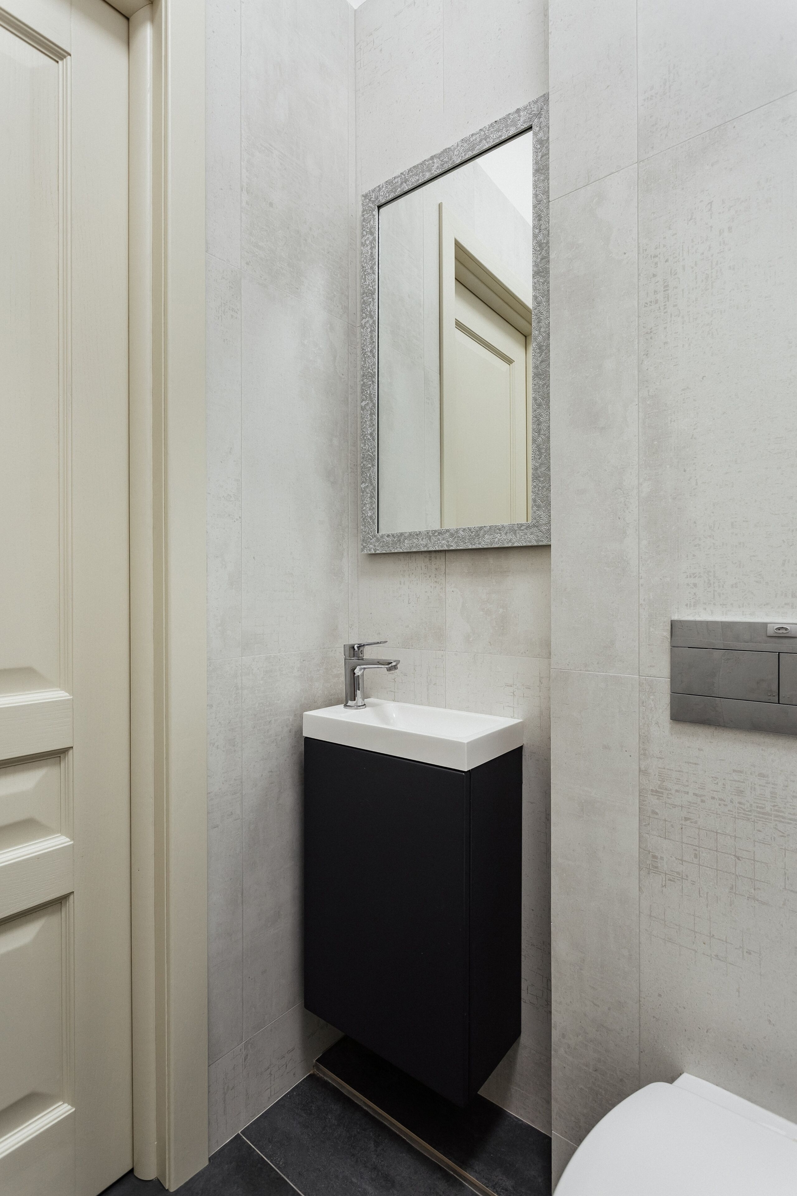 A bathroom with a white sink, dark cabinet, and a mirror with a gray frame.