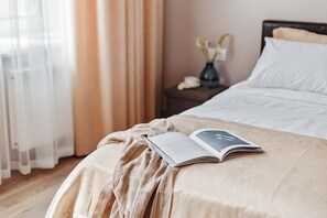 A neatly made bed with a book and a striped blanket, a vase with flowers, and a nightstand with a lamp. - Feeria Apartment Deribasovskaya (Odesa)