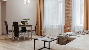 A modern living room with a dining area, a brick wall, and a large window with sheer curtains.