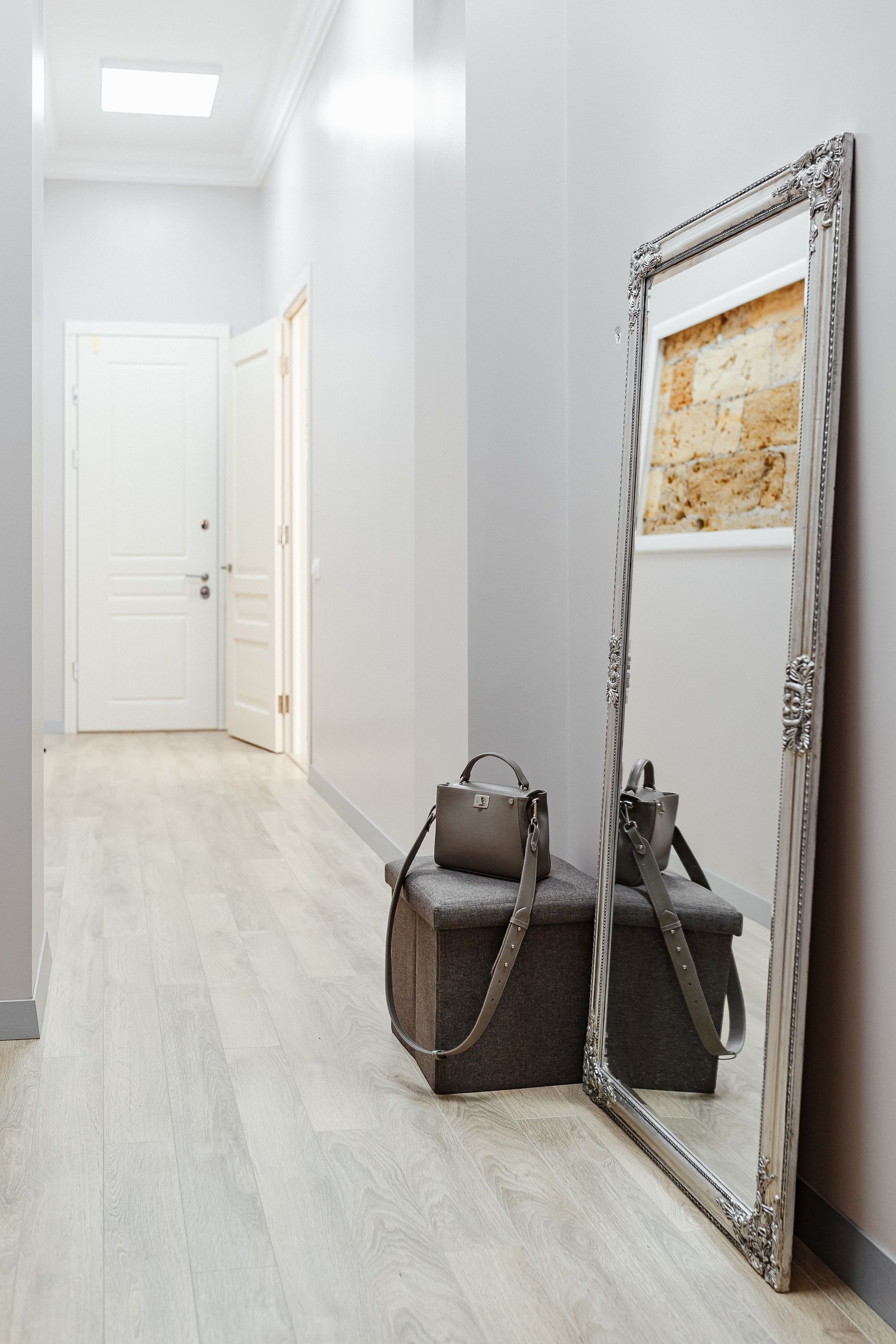 A hallway with a large mirror, a grey bench, and a door at the end.