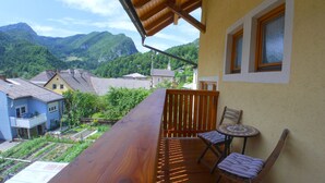 Una terraza de madera con dos sillas y una mesa, con vistas a un pueblo con casas y montañas.