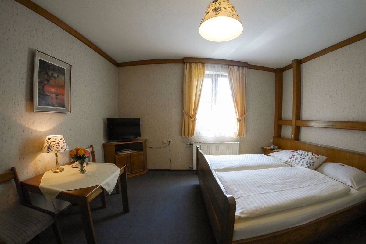 Una habitación de hotel con cama, escritorio con silla, televisión y ventana con cortinas.