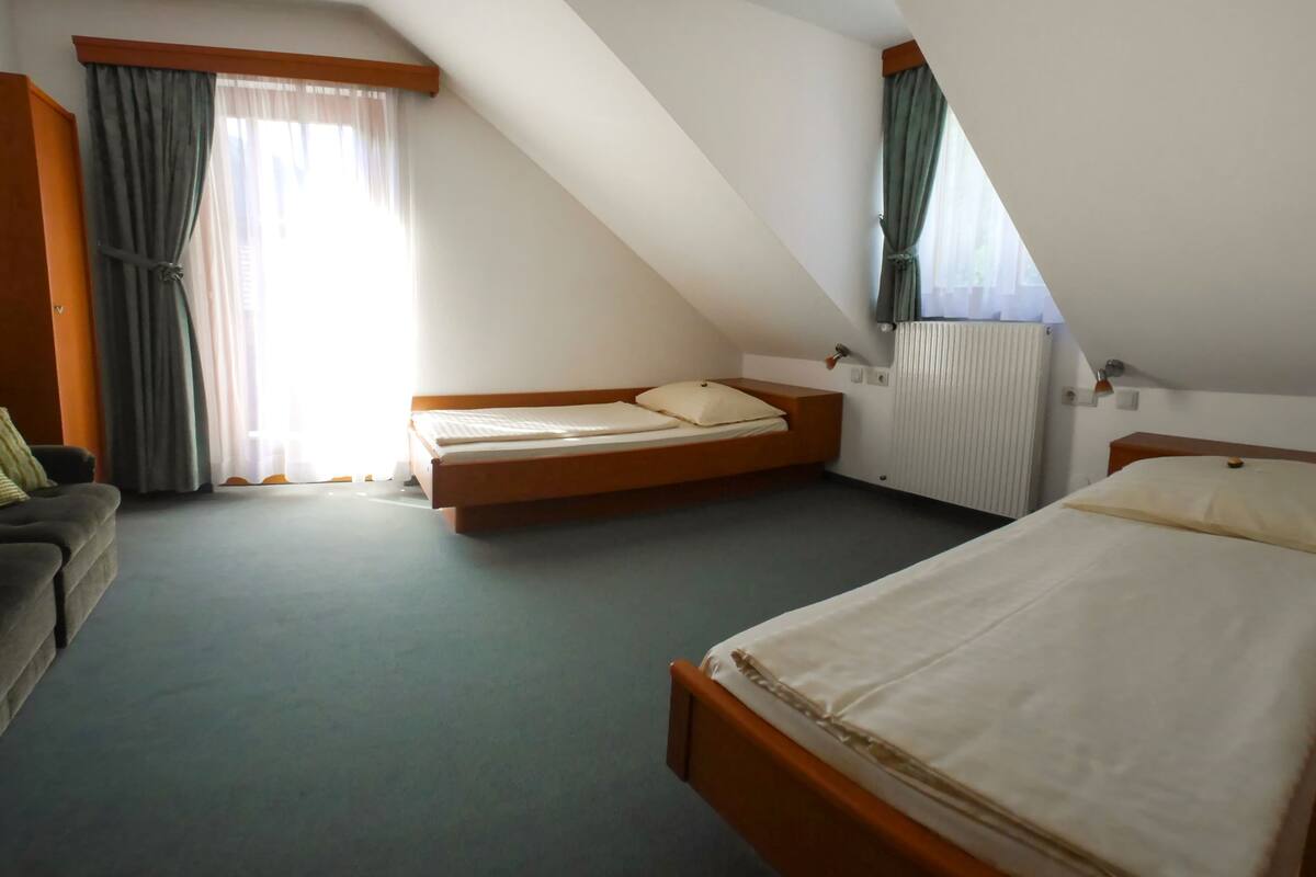 Habitación con dos camas, un sofá y un ventanal con cortinas.
