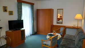 Habitación de hotel con televisión, armario, sofá, sillón, mesa con lámpara y espejo.
