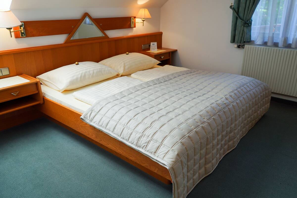 Una cama bien hecha con edredón acolchado, cabecera de madera, lámparas de noche y mesita de noche.