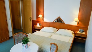 Habitación de hotel con cama, dos mesitas de noche, una silla, una mesa pequeña con un florero y un espejo en la pared.