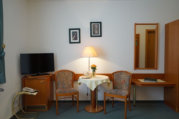 A hotel room with a television, two chairs, a small table with a lamp, and two framed pictures on the wall. - Pension Besser (Eisenkappel-Vellach)