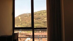A hotel room with a large window offering a view of a hilly landscape and buildings. - Hotel Ruta de la Plata (Lena)
